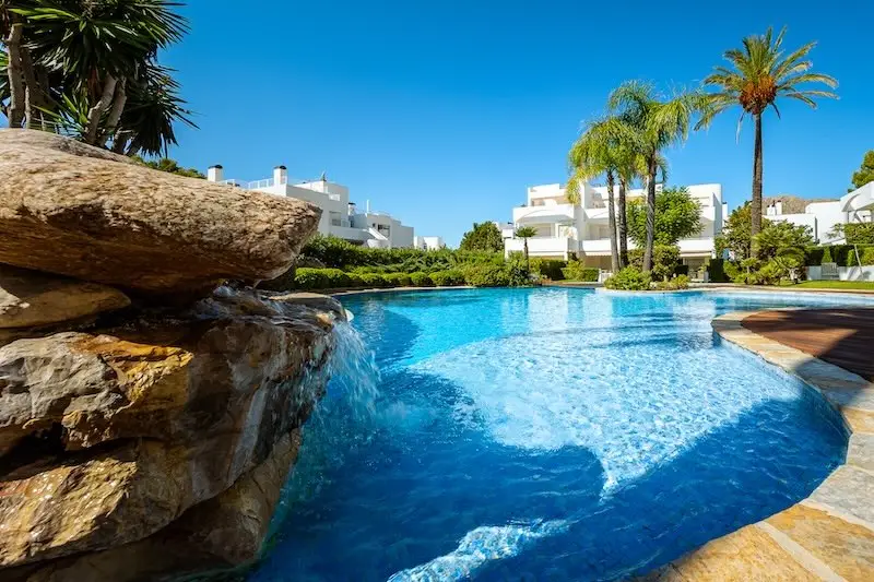 Swimming pool with waterfall and palm trees in a Mediterranean residential complex